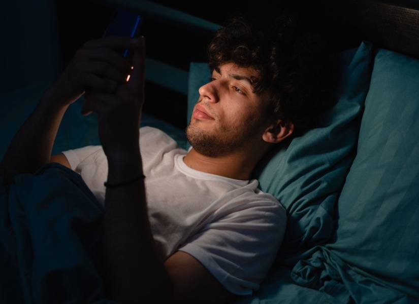 Imagen referencial: Joven usando su celular en la cama.