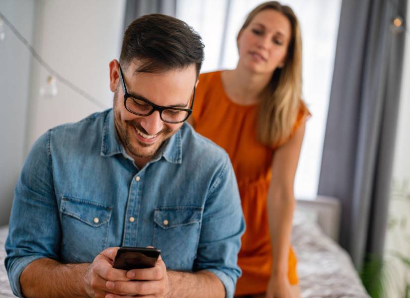 Imagen referencial de hombre chateando con otra persona mientras su pareja está tras él.