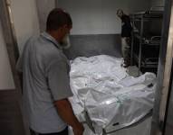 Dos palestinos miran los cadáveres envueltos en bolsas de plástico en la morgue.