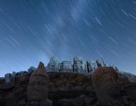 Una imagen de larga exposición muestra meteoros de la lluvia de estrellas de las perseidas surcando el cielo nocturno este domingo, sobre grandes estatuas en la tumba-santuario del rey Antíoco en la cima del monte Nemrut en la discoteca Kahta en Adiyaman (Turquía).