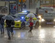 Varias personas se protegen de la lluvia en la Plaza de España de Barcelona este lunes cuando las comarcas de del Garraf y del Barcelonès, en Barcelona, están en aviso rojo de la Agencia Estatal de Meteorología.