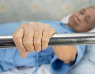 Una mujer mayor acostada en la cama mientras sostiene una barandilla en el hospital
