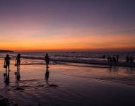 Imagen referencial de personas en la playa durante el atardecer.