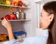 Imagen referencial de mujer viendo frutas y verduras en el refrigerador.