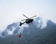 Un helicóptero con sistema bambi bucket lleva agua para intentar apagar un incendio forestal en Cuenca.