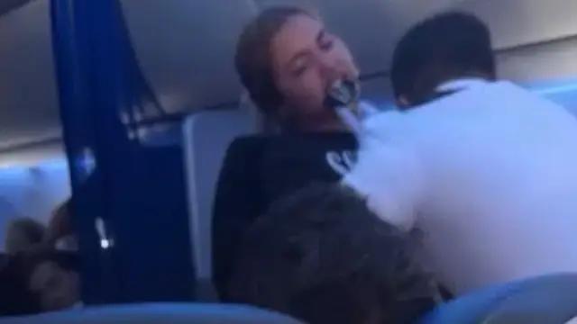 Mujer arrancando parte de la camisa de un asistente de vuelo con un mordisco.