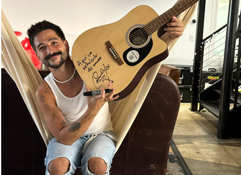 Fotografía del cantante Camilo junto a su guitarra autografiada