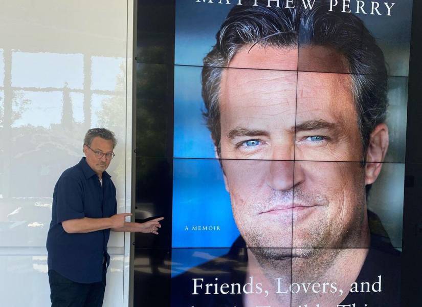 Matthew Perry posando junto a cartel donde muestra la portada de su libro.