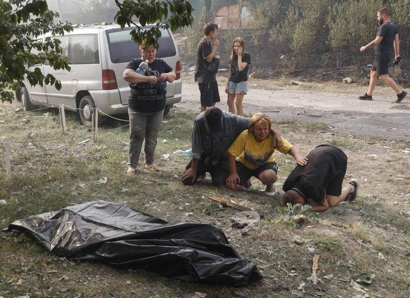 Vecinos lloran junto al cuerpo cubierto de una mujer, cerca del lugar de un ataque con misiles en Cherkaska Lozova, 31 de agosto 2024.