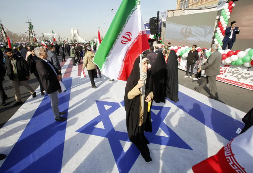 Una mujer iraní sostiene la bandera nacional de Irán mientras camina sobre la bandera de Israel