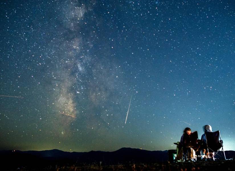 Una pareja observa cómo un meteoro surca el cielo nocturno más allá de la Vía Láctea durante la lluvia de meteoros de las perseidas sobre el lago Kozja.