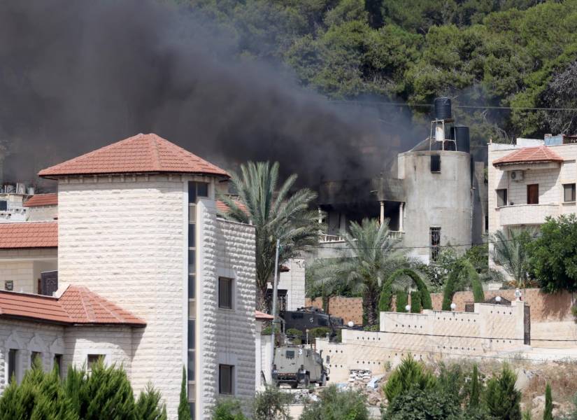 Un vehículo militar israelí circula cerca de un edificio incendiado durante una operación militar israelí