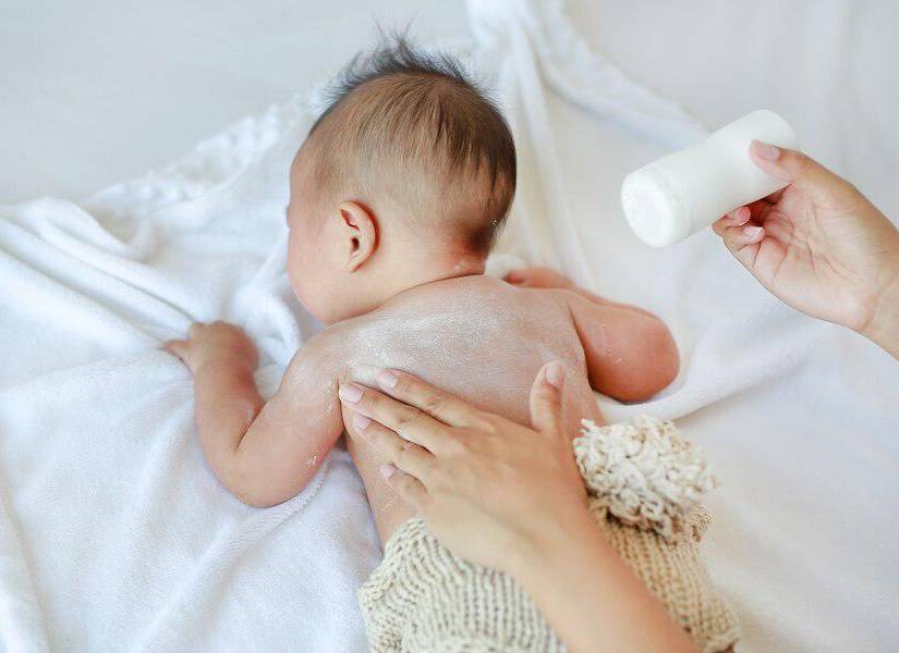 Persona colocando talco a un bebé en su espalda