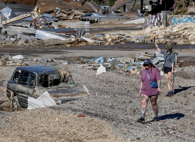 Fotografía de personas caminando junto a un vehículo afectado luego de las inundaciones provocadas por la tormenta tropical Helene.