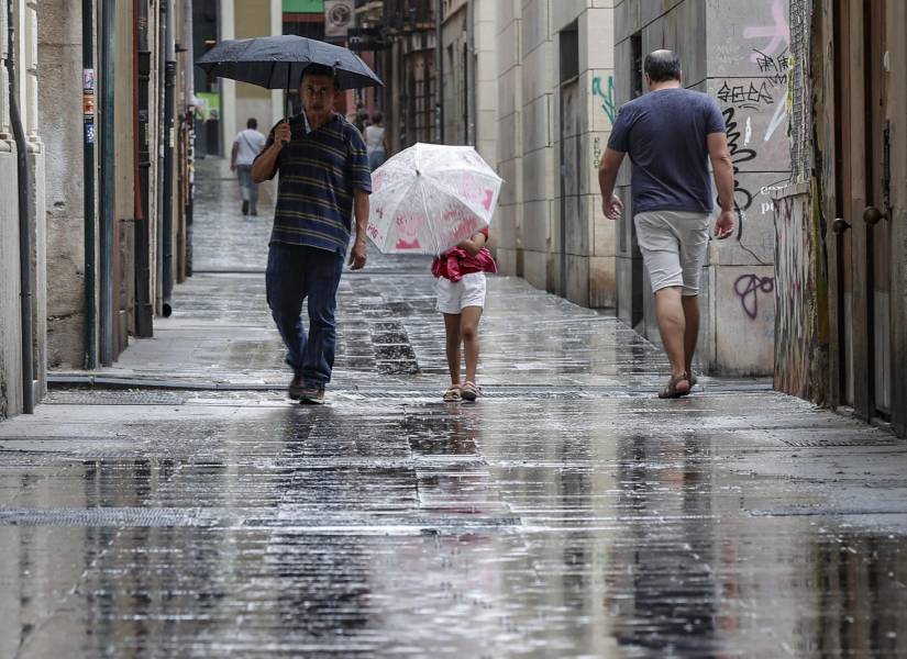 Varias personas caminan bajo la lluvia por una calle del centro de Valencia. EFE/Manuel Bruque