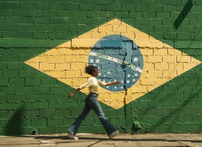 Mujer caminando frente a pared pintada con la bandera de Brasil.