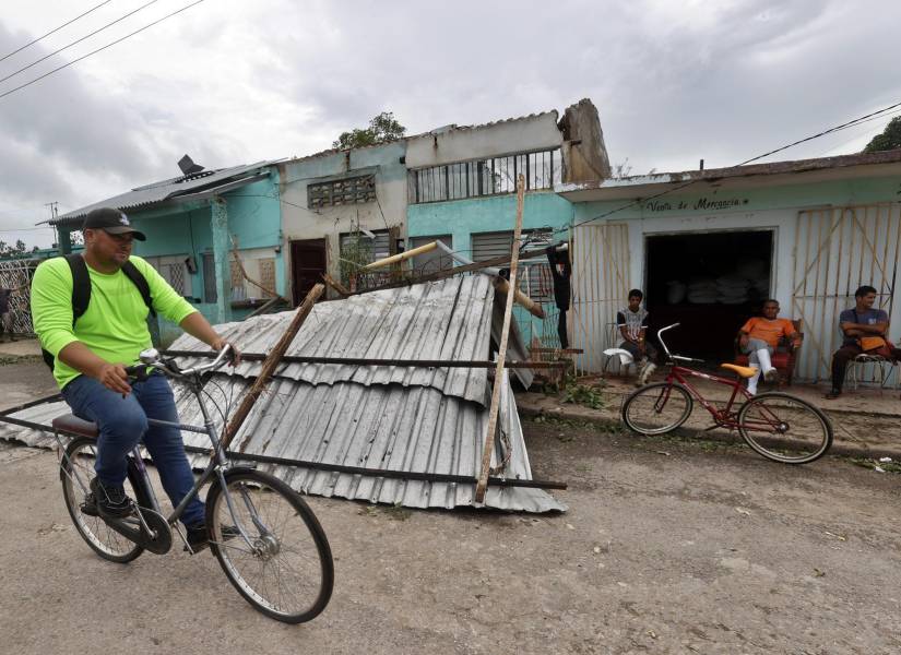 Un hombre transita en bicicleta frente a una vivienda con el techo caído tras el paso del huracán Rafael